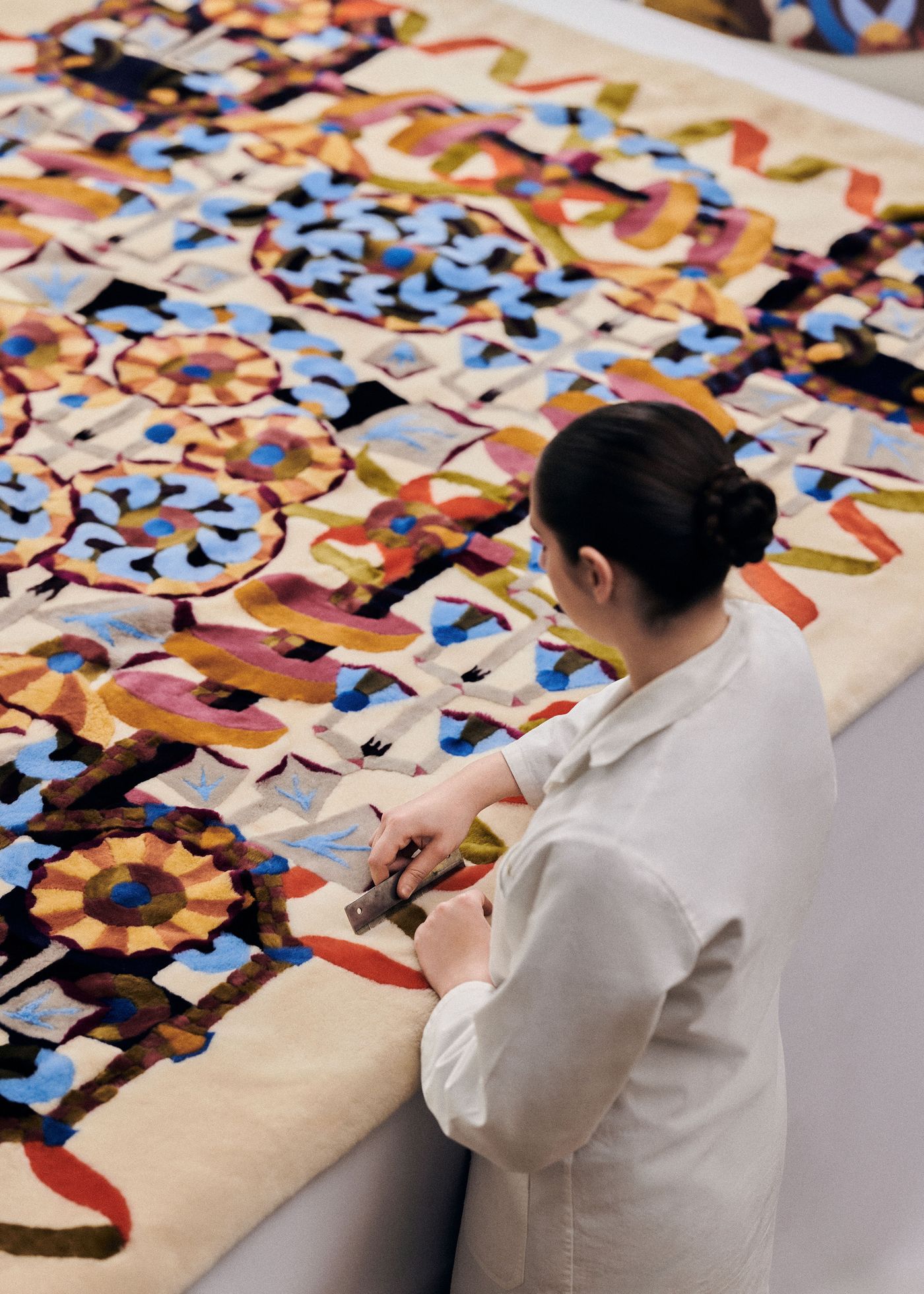 An artisan meticulously working on a large, colorful embroidered tapestry stretched out before her.