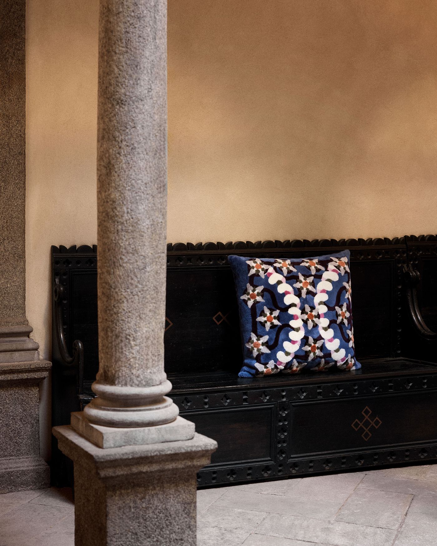 A cozy corner featuring a dark wooden bench adorned with a decorative cushion in bold, colorful embroidery.