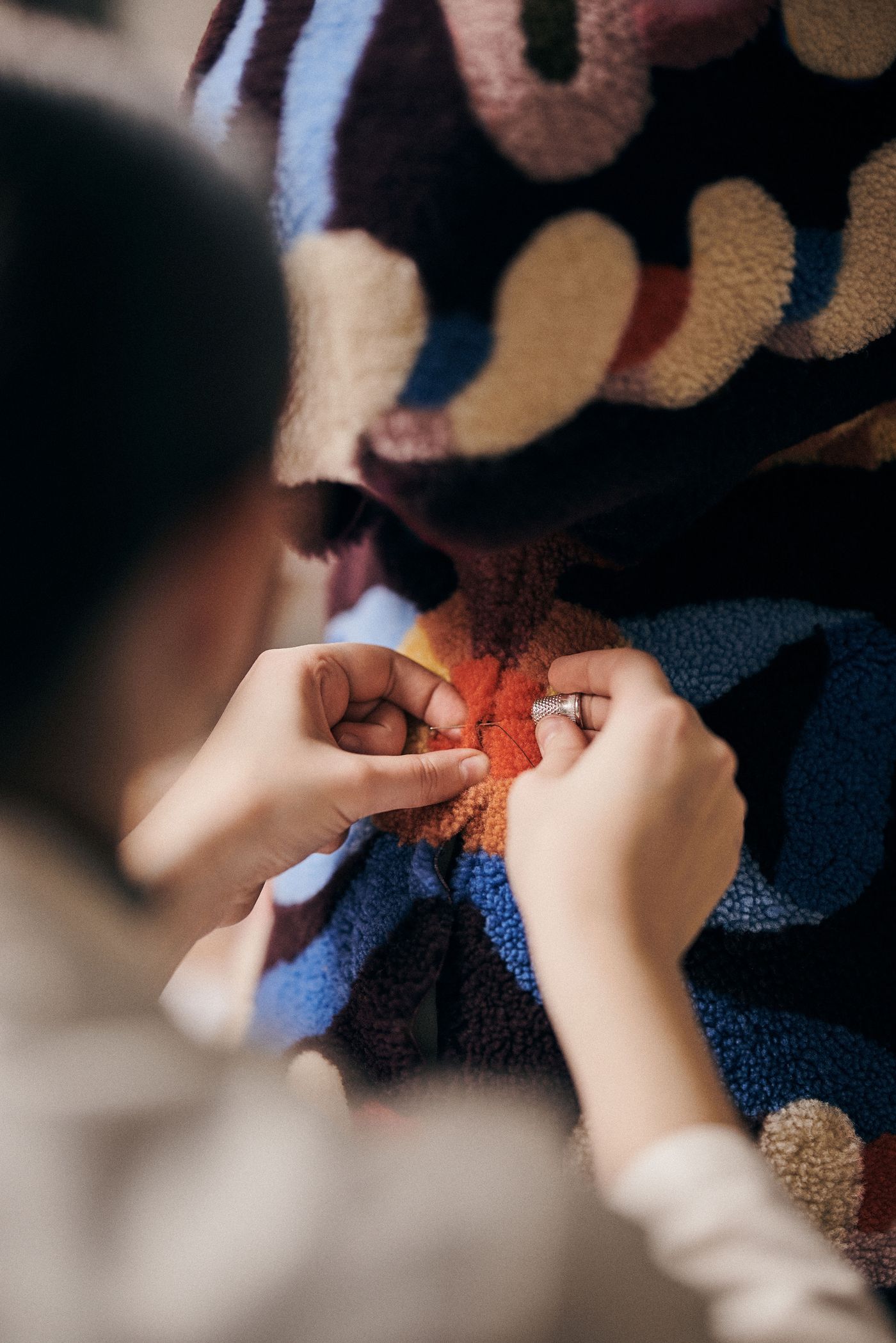 A close-up of a hand stitching vibrant embroidery onto a colorful textile surface.