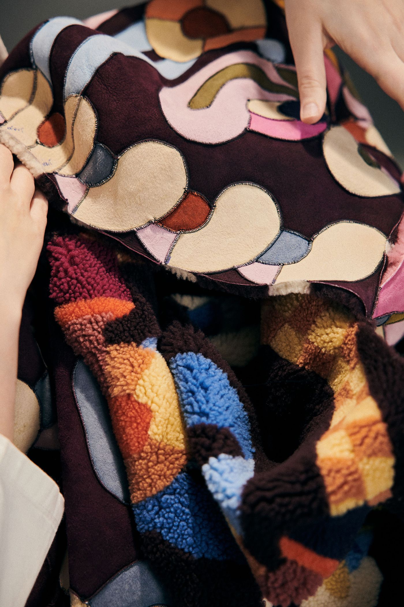 Hands holding and adjusting a richly textured and colorful patchwork of embroidered fabrics.