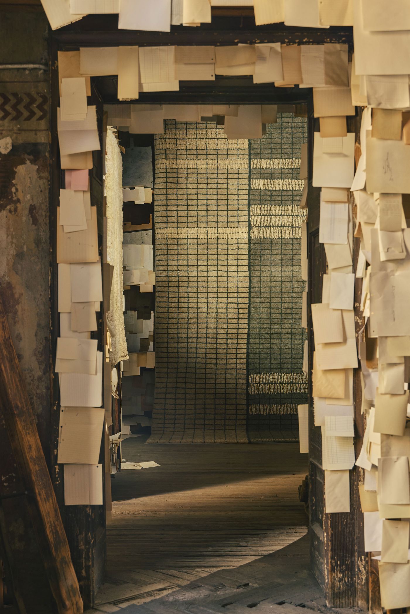A deep, atmospheric hallway lined with pinned paper notes opens onto a large rug with a green and cream grid pattern and hand-stitched textures. 	3.	Third image: A sun-drenched doorway reveals