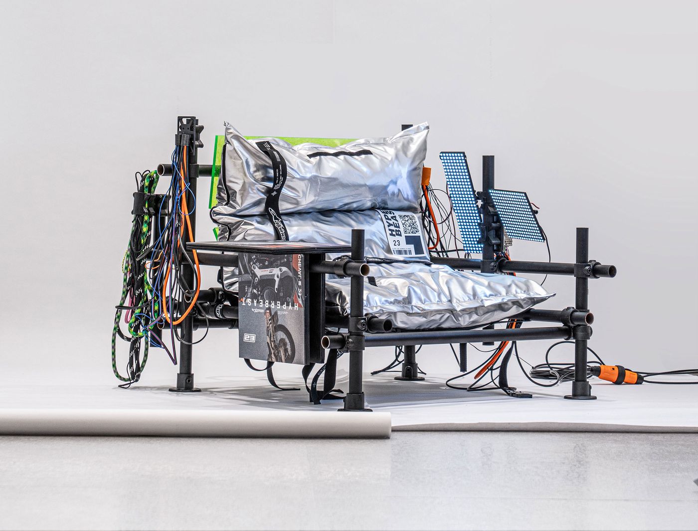 A modern, industrial-style chair with metallic cushions and colorful cables, showcasing an innovative design in a minimalist setting. A modern, industrial-style chair with metallic cushions and colorful cables, showcasing an innovative design in a minimalist setting.