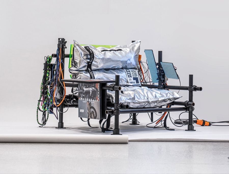 A modern, industrial-style chair with metallic cushions and colorful cables, showcasing an innovative design in a minimalist setting.