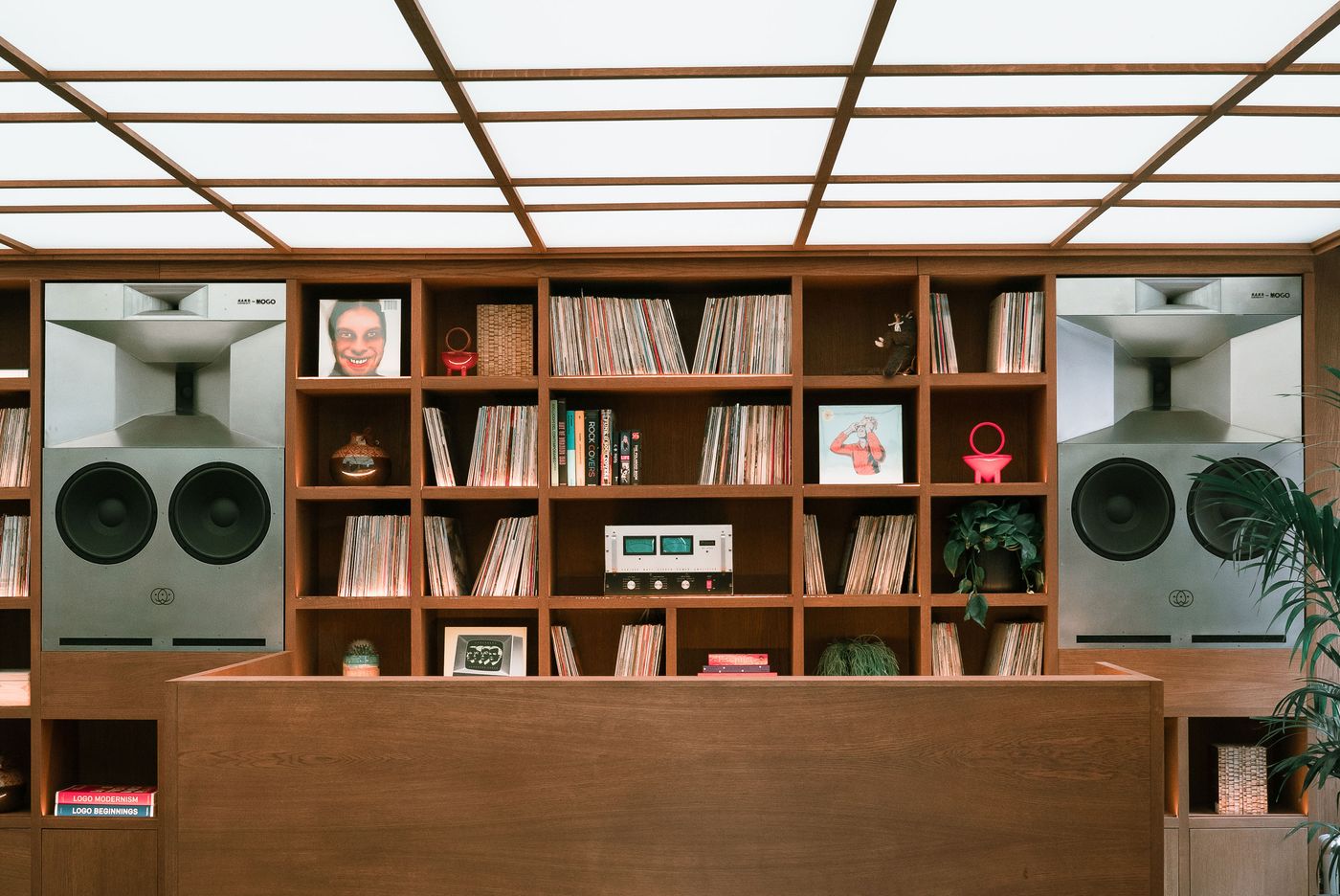 A wooden reception desk in front of shelves filled with vinyl records and large speakers, against a softly illuminated ceiling. A wooden reception desk in front of shelves filled with vinyl records and large speakers, against a softly illuminated ceiling.