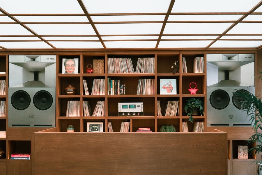 A wooden reception desk in front of shelves filled with vinyl records and large speakers, against a softly illuminated ceiling.