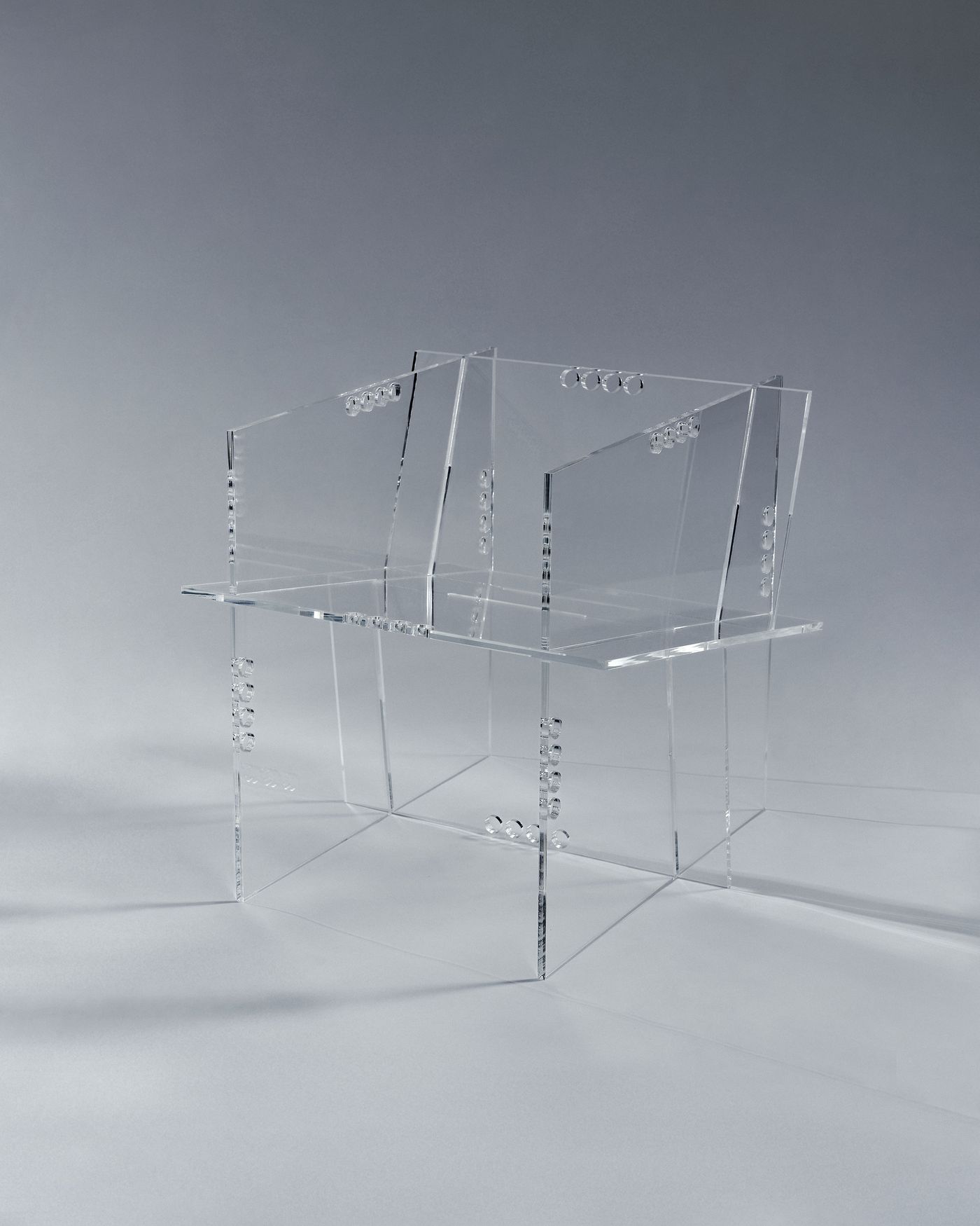 Clear acrylic armchair with angular planes and circular joint details, floating like a ghostly sculpture.