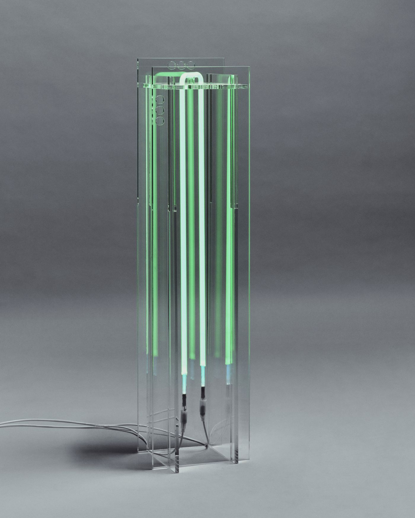 Vertical acrylic lamp glowing in electric green, a futuristic totem of light.