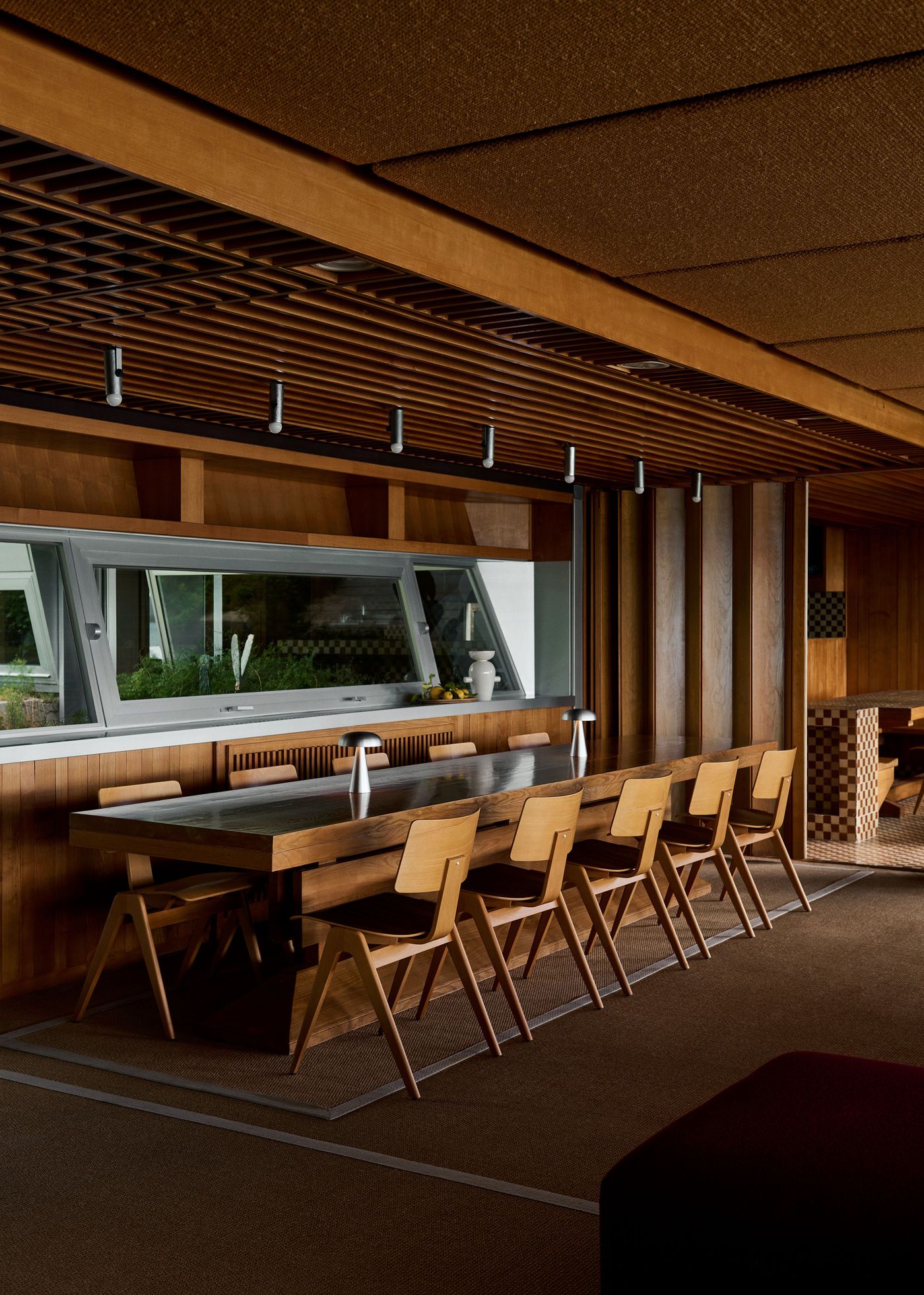 A warm, wood-rich dining space features a row of minimalist Como lamps by Space Copenhagen for &Tradition, blending function and form in perfect harmony.