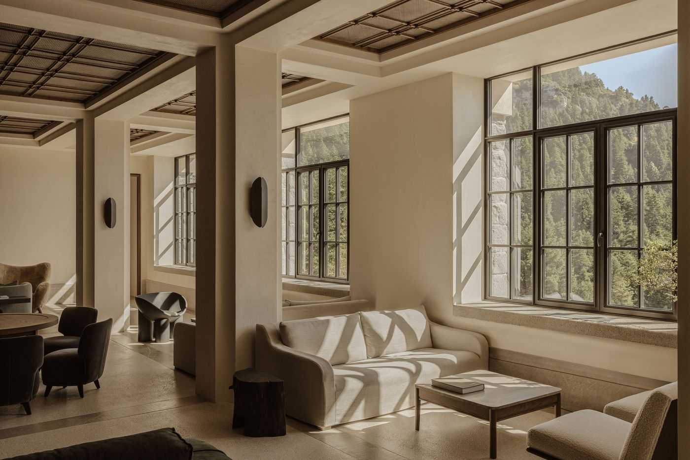 Lounge area with cream sofas and panoramic forest views, bathed in soft light through black-framed windows. Lounge area with cream sofas and panoramic forest views, bathed in soft light through black-framed windows.