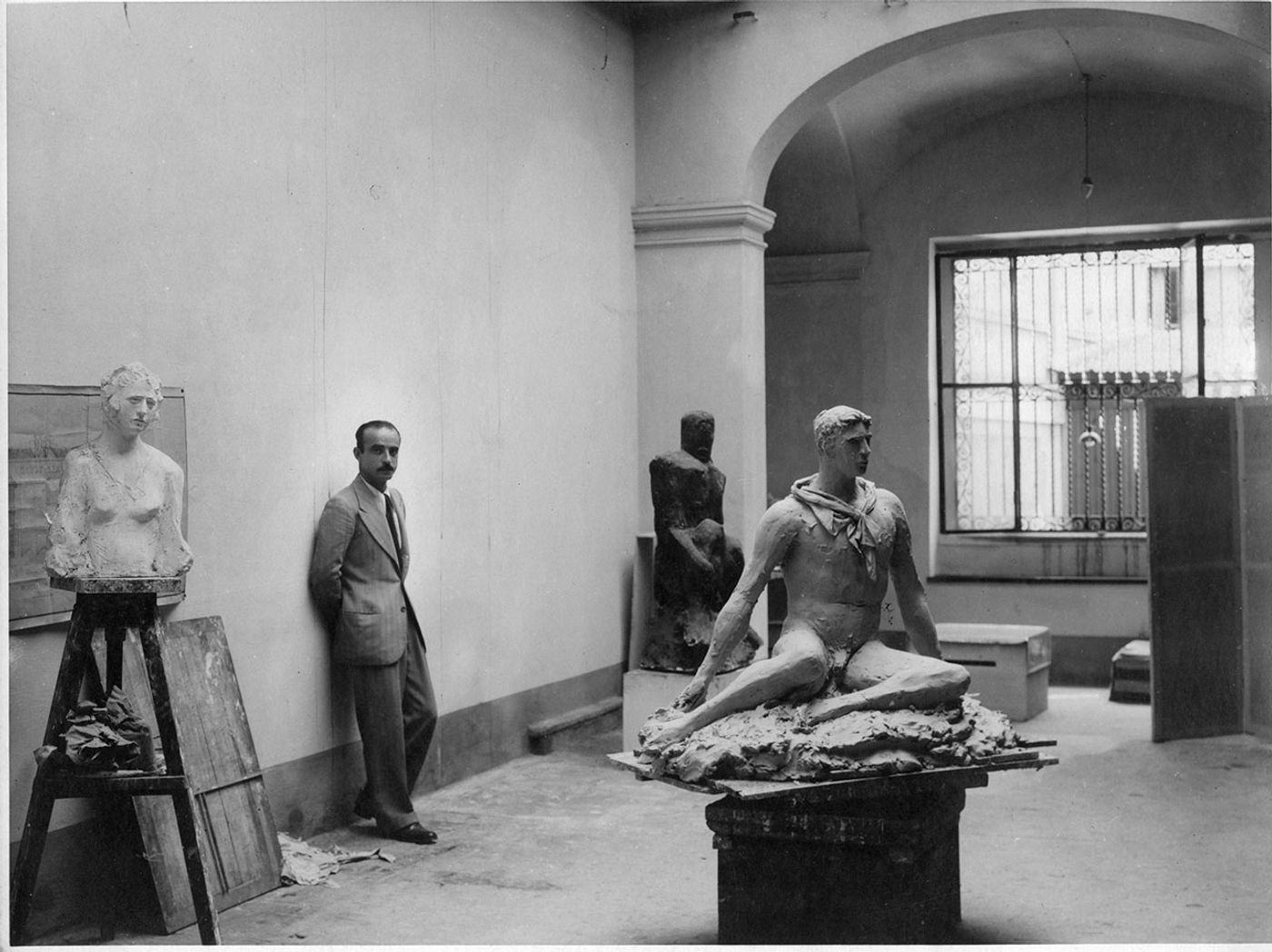 Lucio Fontana in his studio at via De Amicis, Milan 1933. From left to right: Busto di Signorina, Uomo Nero, Uomo seduto (or Atleta in Attesa or Discobolo) for the art works © Fondazione Lucio Fontana © Fondazione Lucio Fontana, Milano by SIAE 2018.