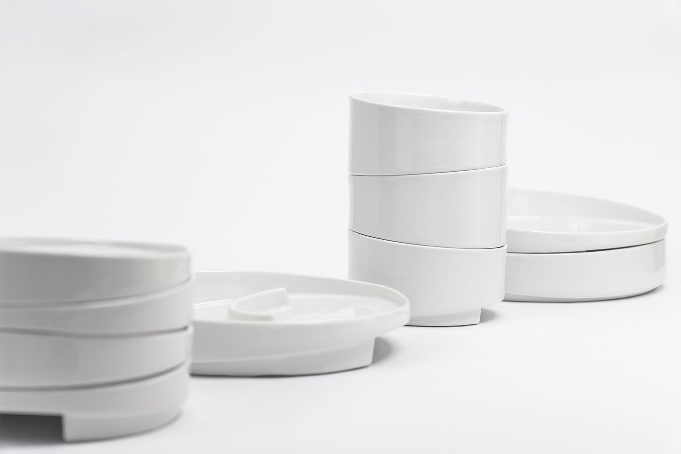 Minimalist white ceramic tableware with organic, asymmetric forms, stacked neatly on a white background.