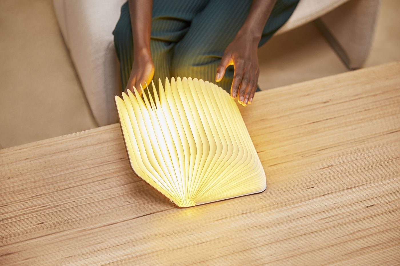 A half-open Lito Lumio lamp sits on a wooden table, resembling a glowing book in the process of being read.