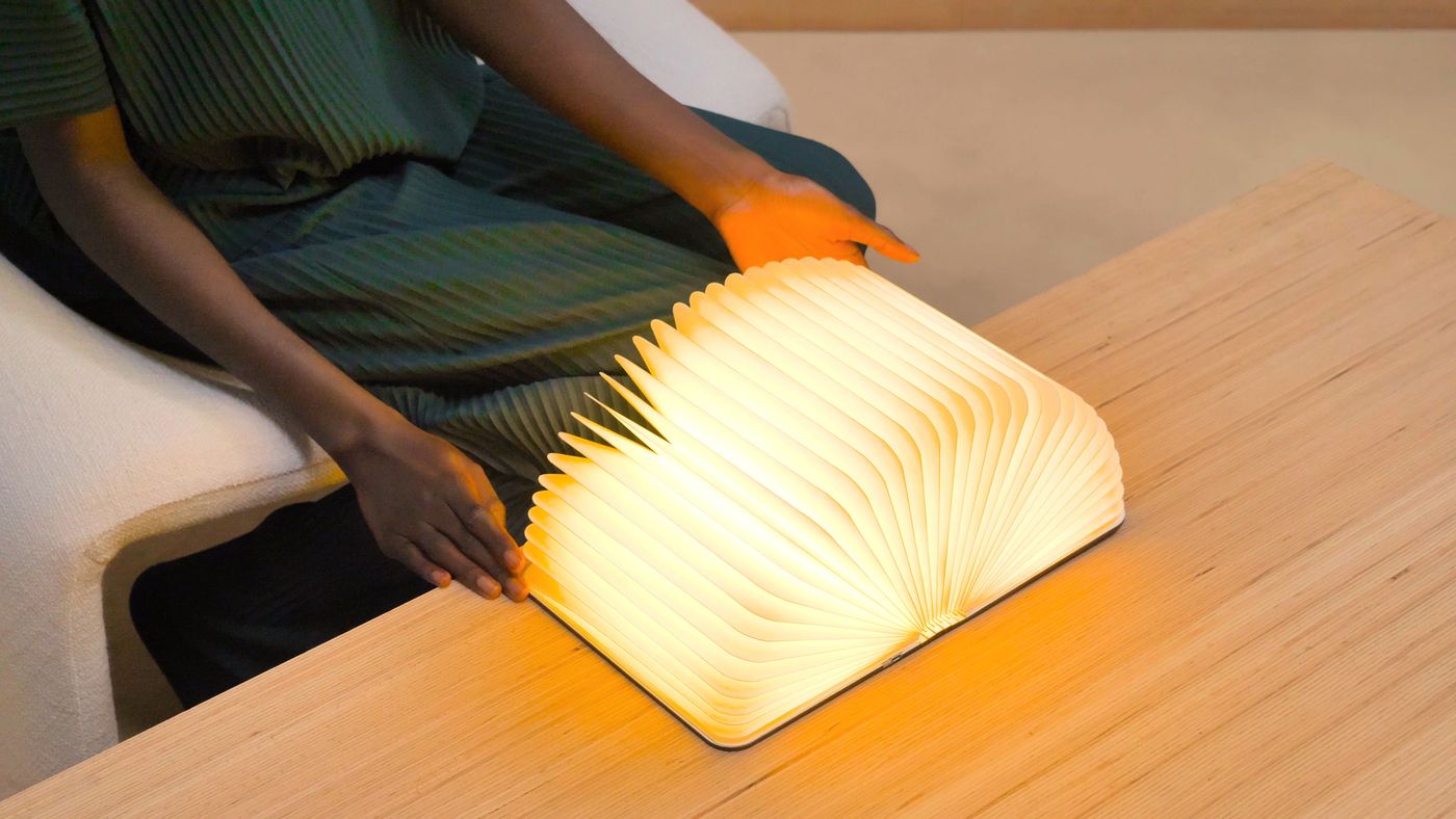 A fully open Lito Lumio lamp rests on a table, its pages fanned out into a dramatic circular form, radiating light across the wood surface.