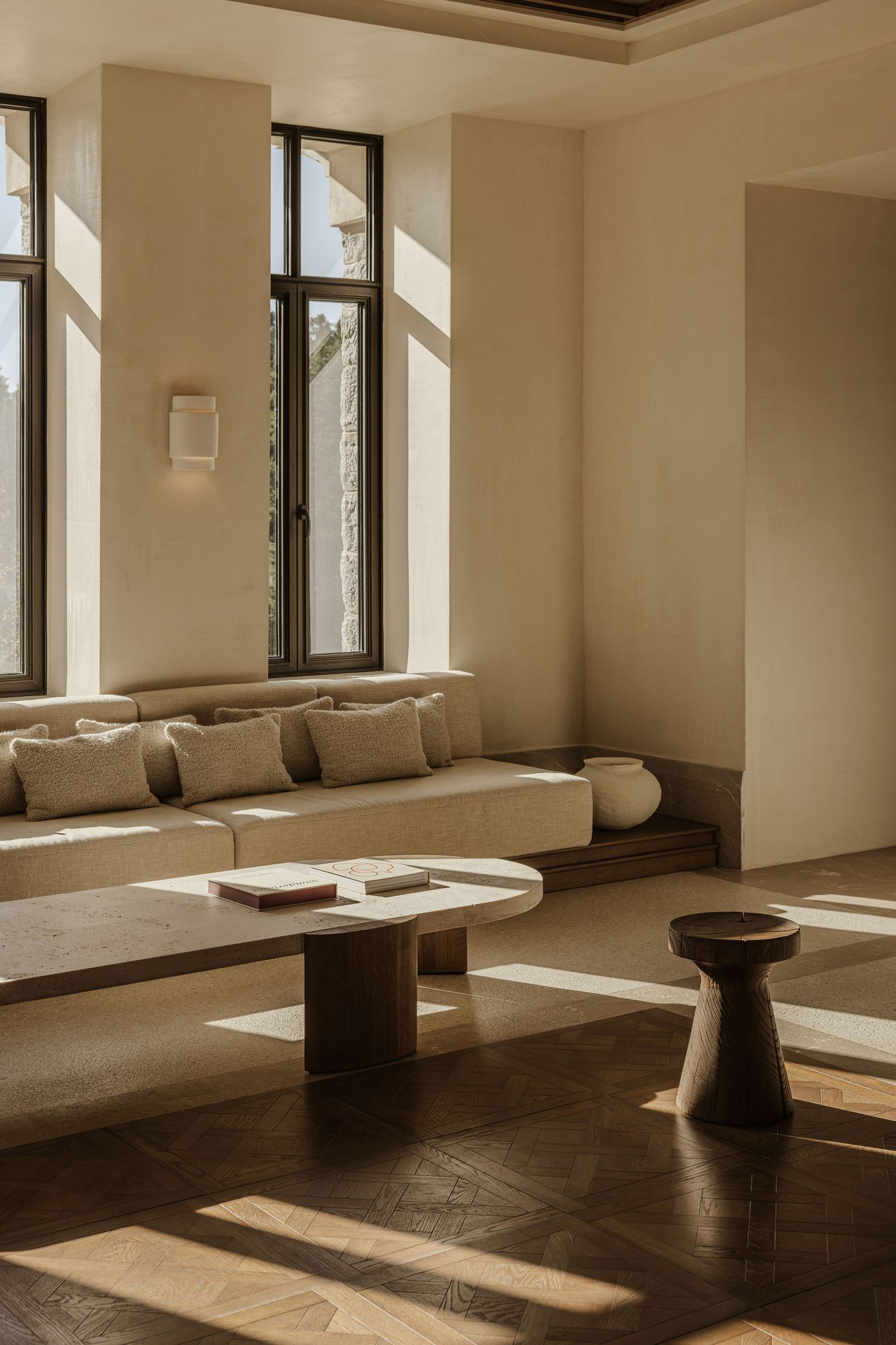 Lounge corner with a long built-in linen sofa, textured cushions, and a travertine coffee table bathed in golden sunlight. Lounge corner with a long built-in linen sofa, textured cushions, and a travertine coffee table bathed in golden sunlight.