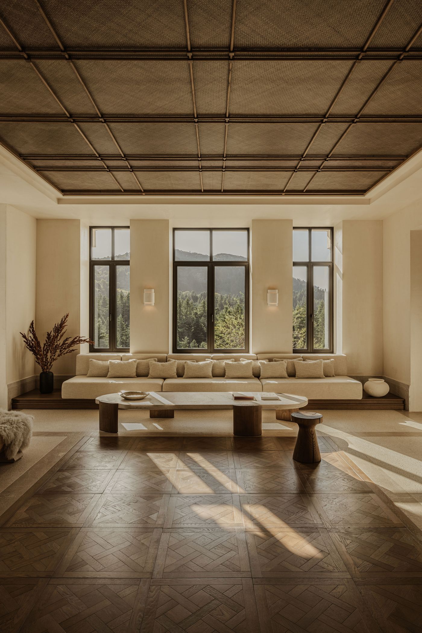 Expansive lounge framed by five large windows overlooking the Arcadian forest, anchored by a long low sofa, sculptural coffee tables, and intricate parquet flooring. Expansive lounge framed by five large windows overlooking the Arcadian forest, anchored by a long low sofa, sculptural coffee tables, and intricate parquet flooring.