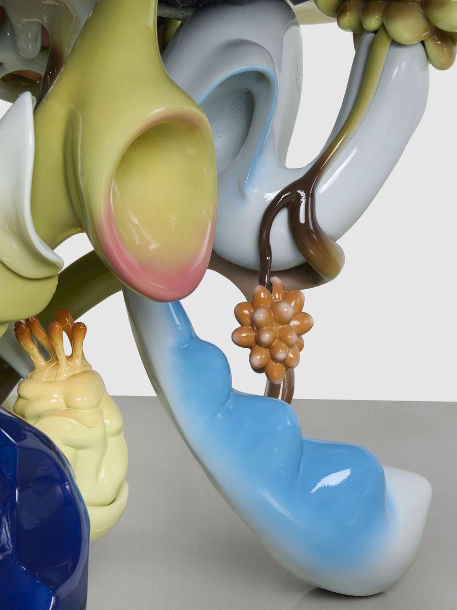 Close-up of the table’s sculptural base showcasing hyper-detailed glossy elements—bulbous yellow forms, curling blue and brown tendrils, and clusters of rounded orange nodules—evoking a dreamlike ecosystem frozen in time. Close-up of the table’s sculptural base showcasing hyper-detailed glossy elements—bulbous yellow forms, curling blue and brown tendrils, and clusters of rounded orange nodules—evoking a dreamlike ecosystem frozen in time.