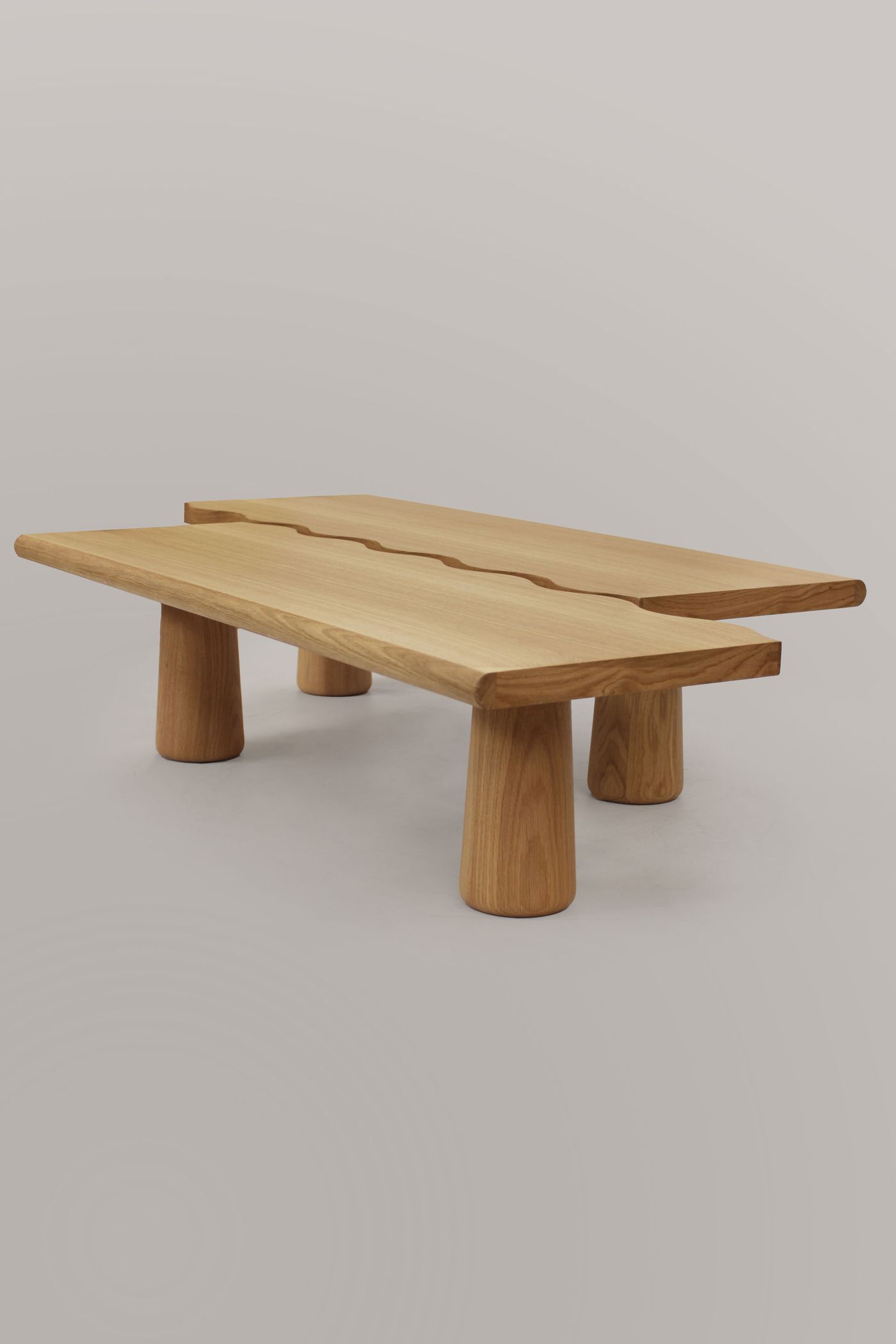 A minimalist wooden coffee table by Gonçalo Campos features an irregular, organic-shaped top crafted from light-toned wood. Supported by thick, cylindrical legs, its form is both playful and sculptural. The clean lines and natural material reflect a contemporary design sensibility, emphasizing craftsmanship and unique spatial presence.