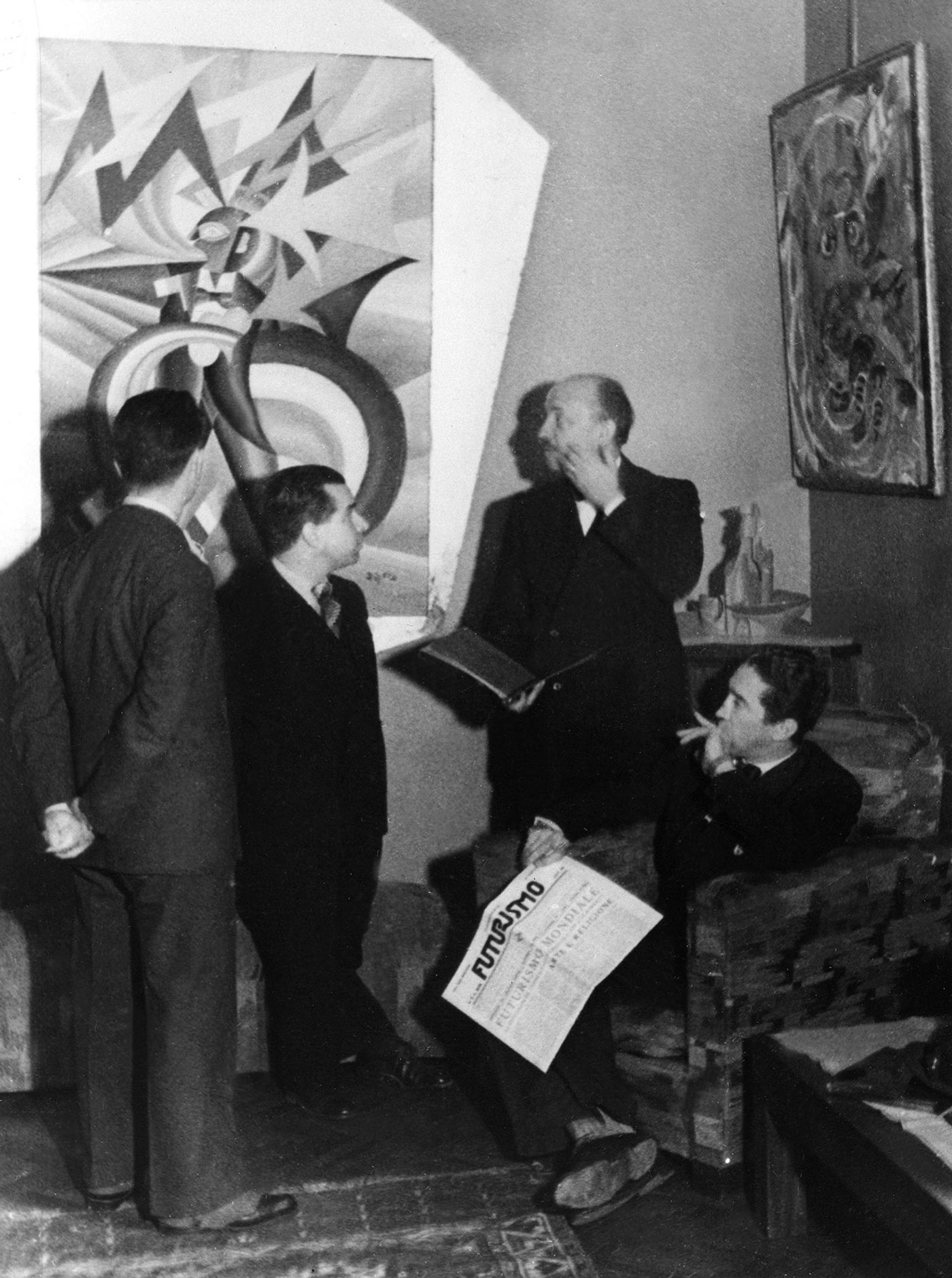 Filippo Tommaso with the editorial team of the magazine 'Futurismo'. From right: Mino Somenzi, Filippo Tommaso Marinetti, Enrico Prampolini and Bruno G. Sanzin (back) In the photo the work Marinetti temporale patriottico, Ritratto psicologico (1924) by Fortunato Depero - For the work © Fortunato Depero by SIAE 2018 Photo: Felix H. Man - Koester - 1931 Ullstein Bild - Felix H. Man /Archivi Alinari, Firenze.