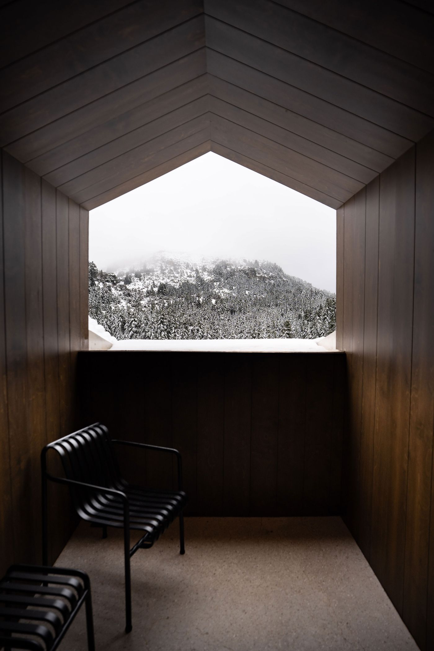 Framed mountain view from a dark wood balcony nook at Manna Hotel in winter.