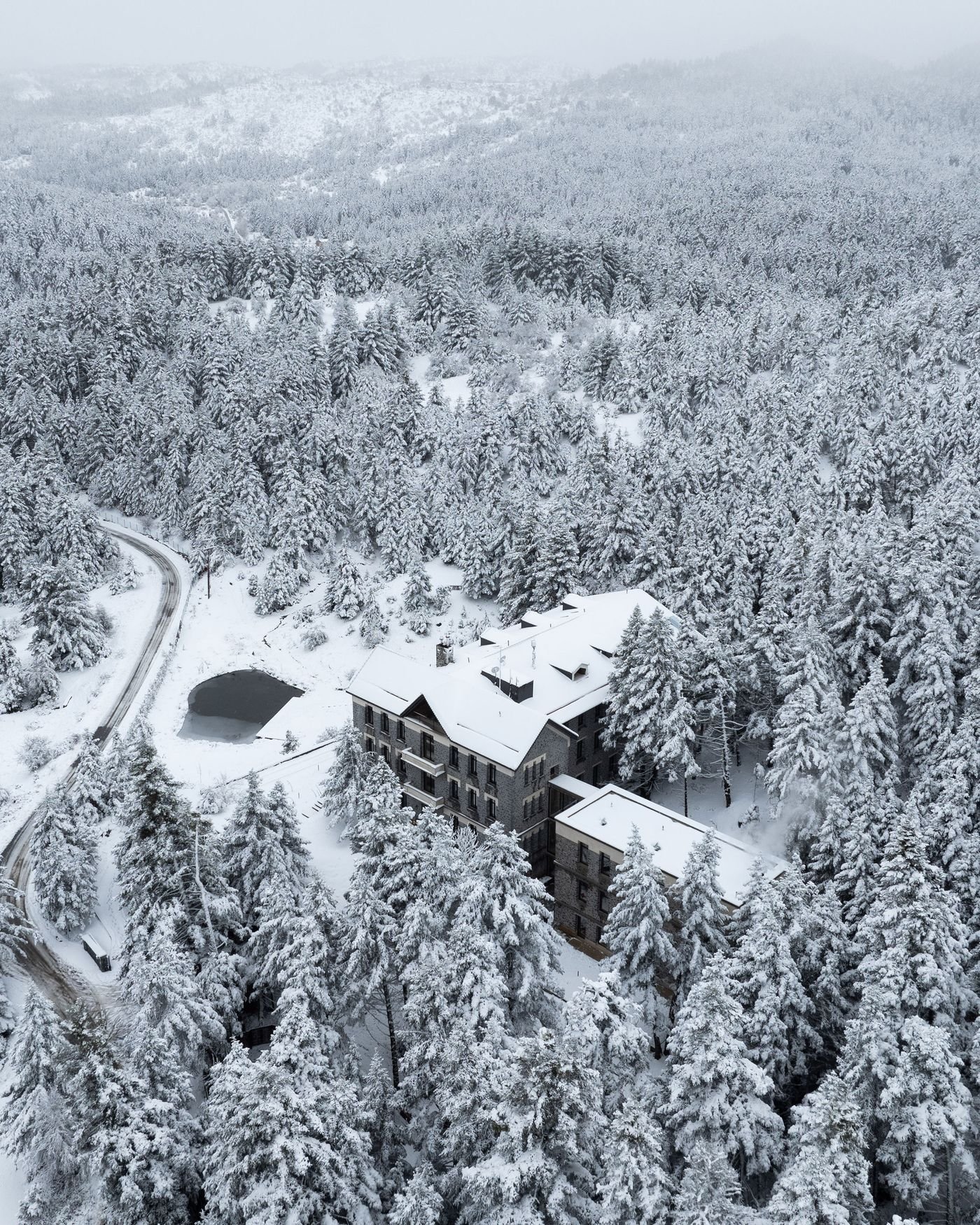 Aerial view of Manna Hotel nestled in a snowy pine forest landscape in Arcadia.