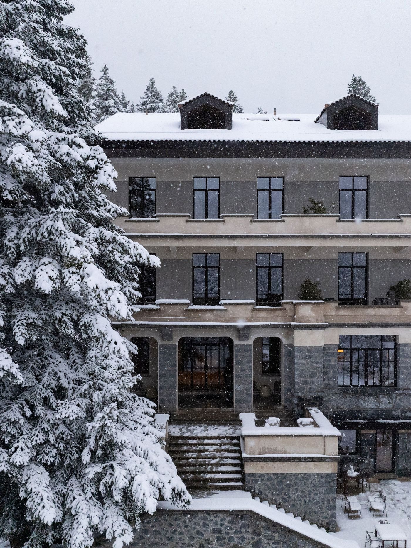 Snow gently falling in front of the stone façade of Manna Hotel’s main entrance.
