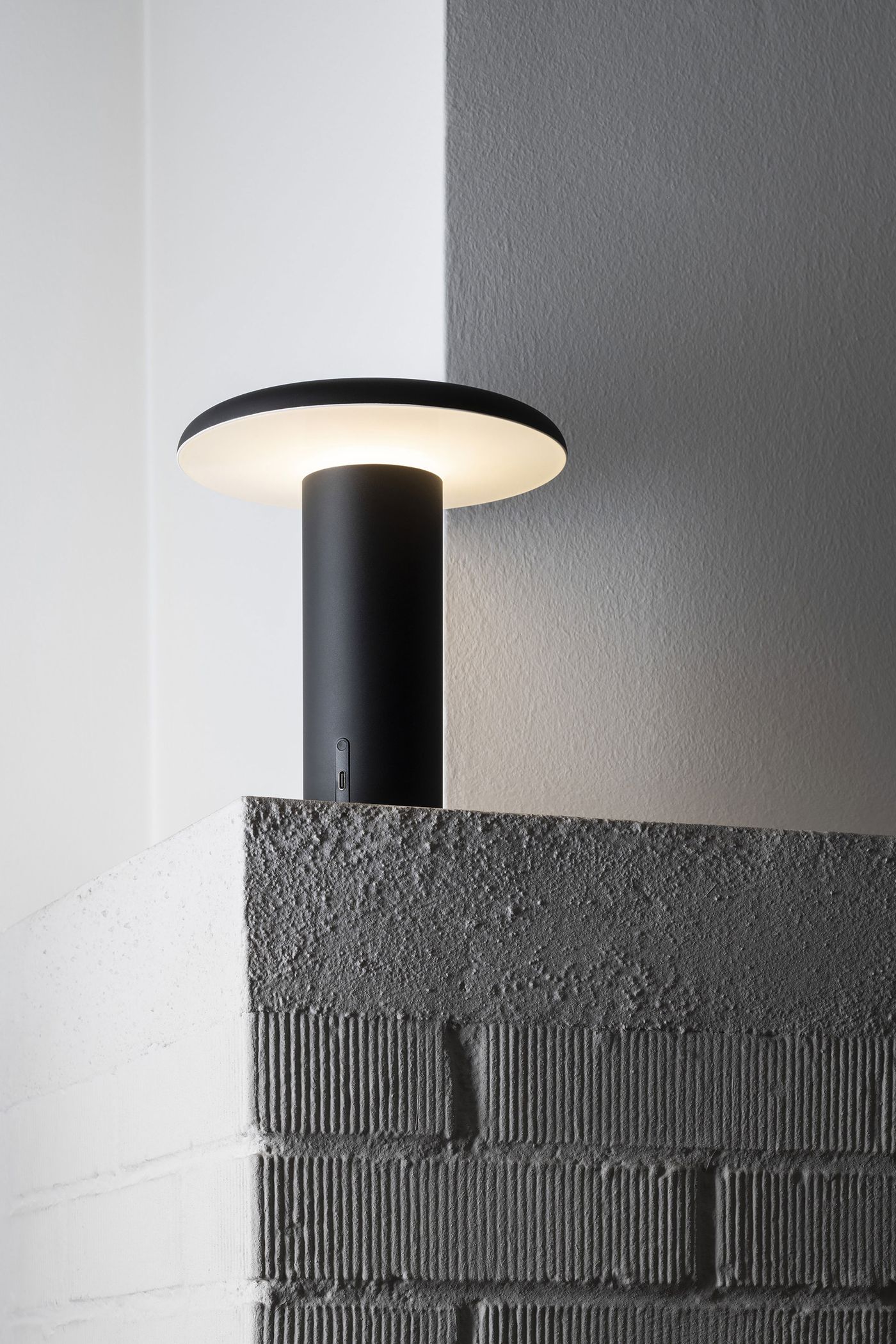 A close-up of the Takku lamp in matte black, glowing softly on the corner of a concrete-textured surface, highlighting its minimalist elegance. A close-up of the Takku lamp in matte black, glowing softly on the corner of a concrete-textured surface, highlighting its minimalist elegance.