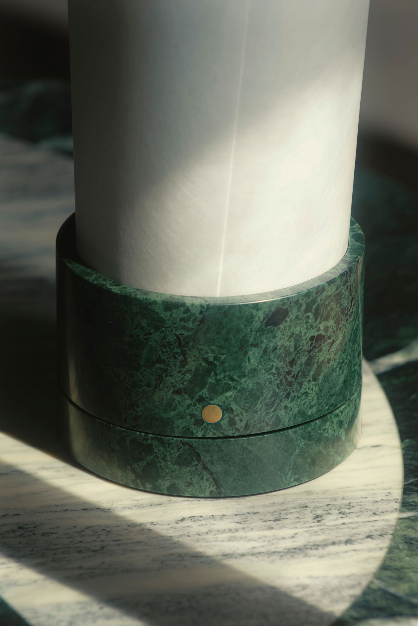 A marble-based table lamp with a paper-like cylindrical shade, softly lit by sunlight.
