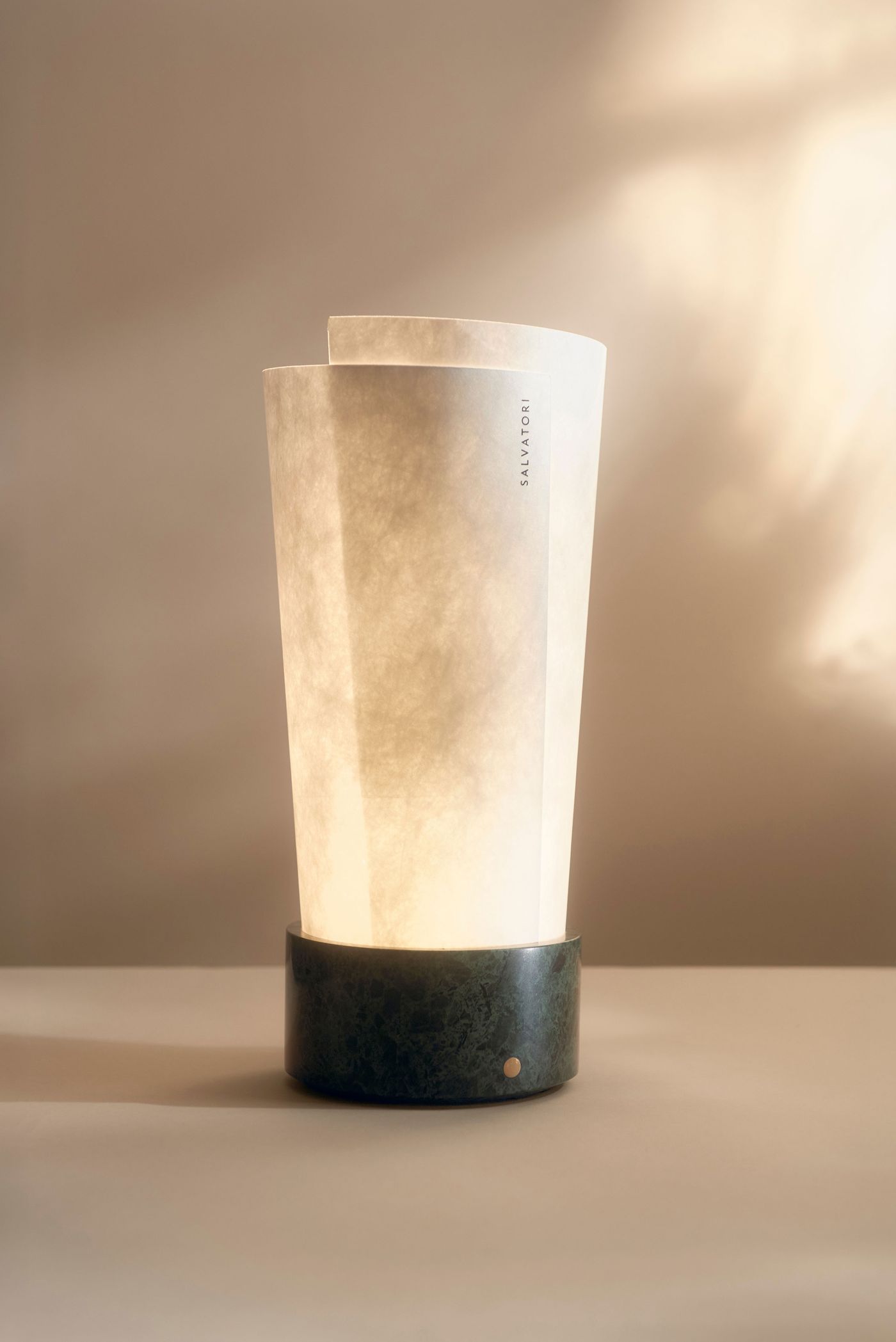 A softly glowing lamp with overlapping vellum layers and a dark green marble base — serene and sculptural.