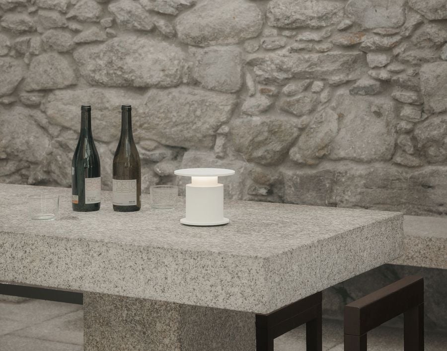 A white w241 Faro lamp emits a gentle glow beside two wine bottles and glasses on a granite table, set against a rustic stone backdrop. A white w241 Faro lamp emits a gentle glow beside two wine bottles and glasses on a granite table, set against a rustic stone backdrop.