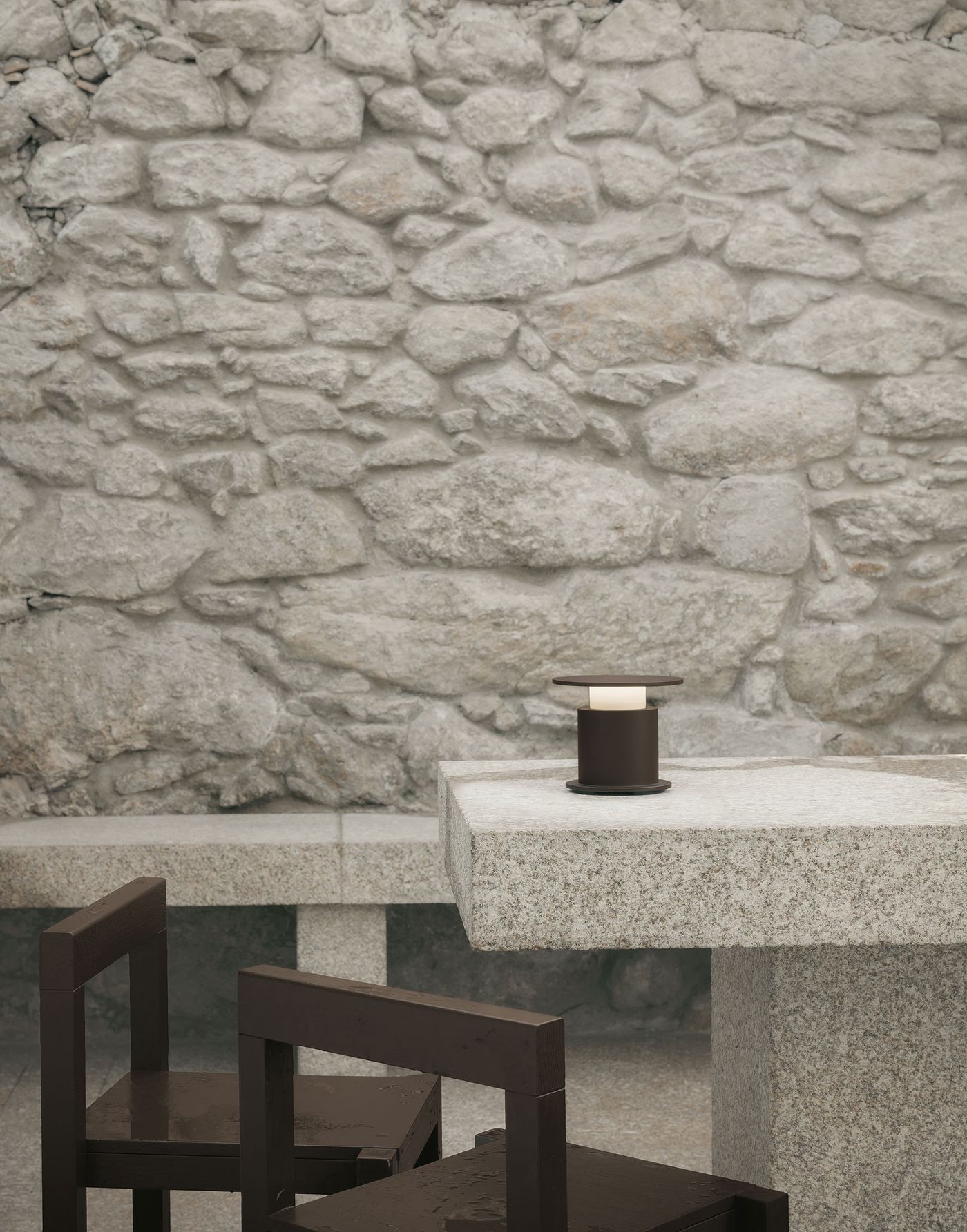 A bronze-toned w241 Faro lamp with a disc top sits on a granite table, backed by a rugged stone wall in a serene outdoor setting. A bronze-toned w241 Faro lamp with a disc top sits on a granite table, backed by a rugged stone wall in a serene outdoor setting.