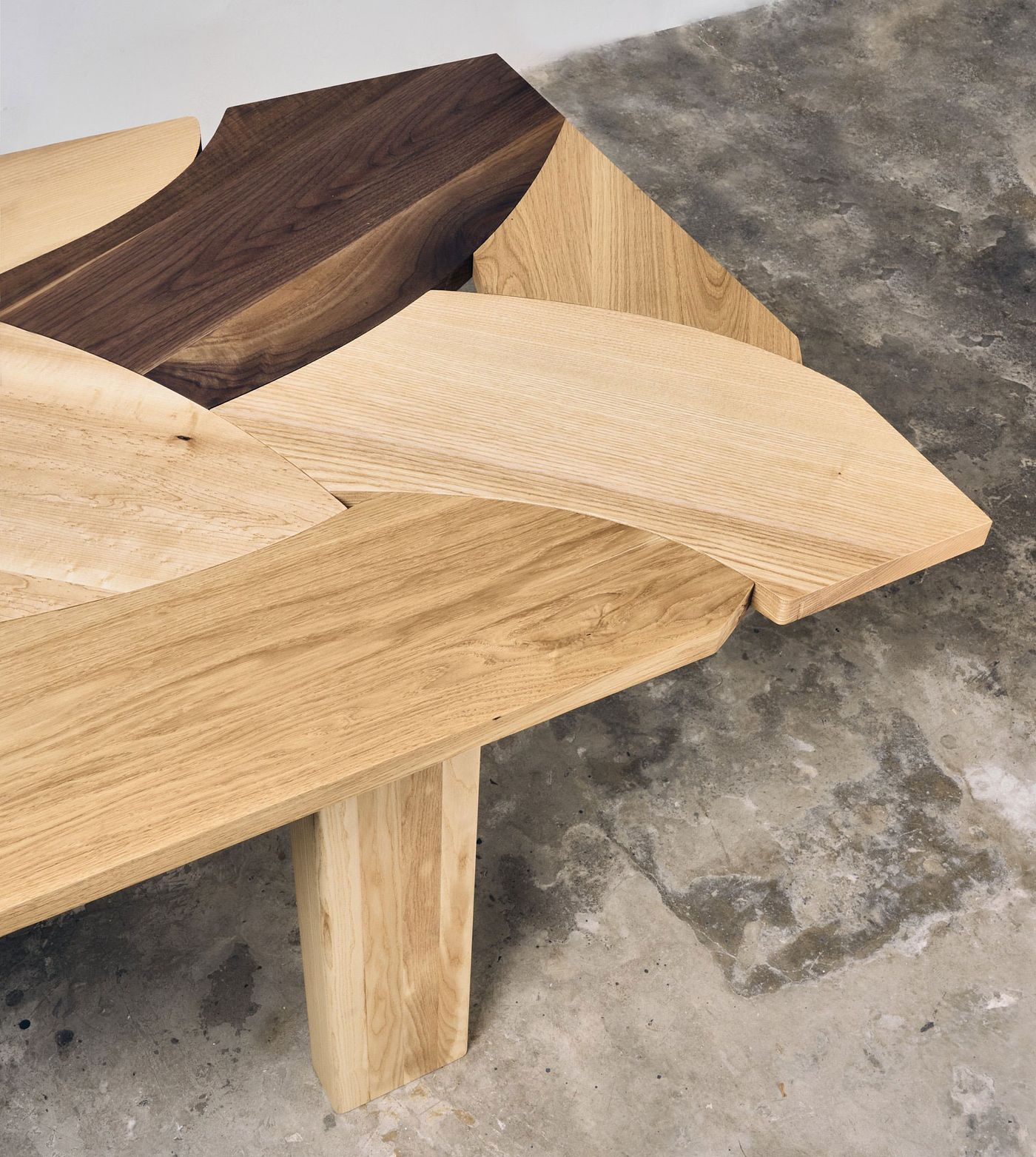 Detail of a wooden table with interwoven wood panels in various shades and grains—fine craftsmanship meets organic rhythm.